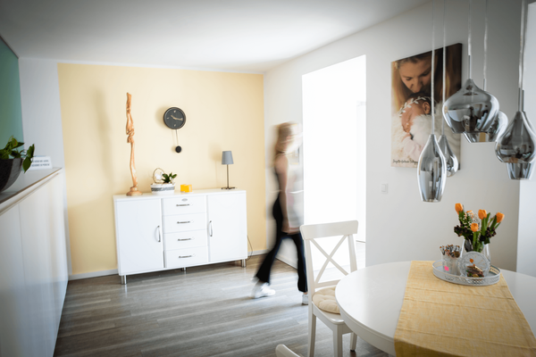 Raum mit Kommode und einem dekorierten Tisch mit Stühlen; Person geht durch den Raum